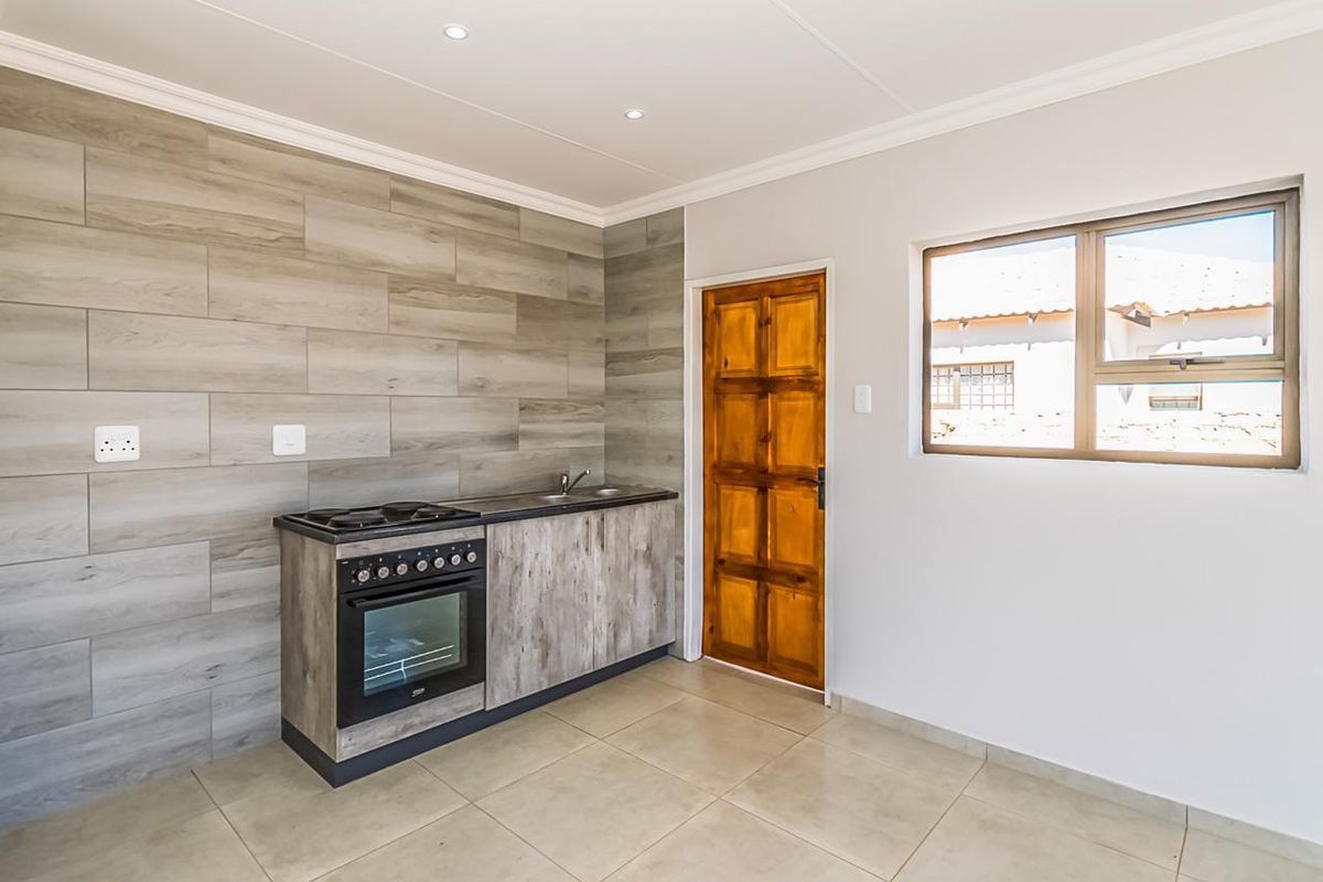 A compact, modern kitchen featuring wood-look cabinetry, a built-in oven and hob, tiled splashback, and neutral floor tiles.