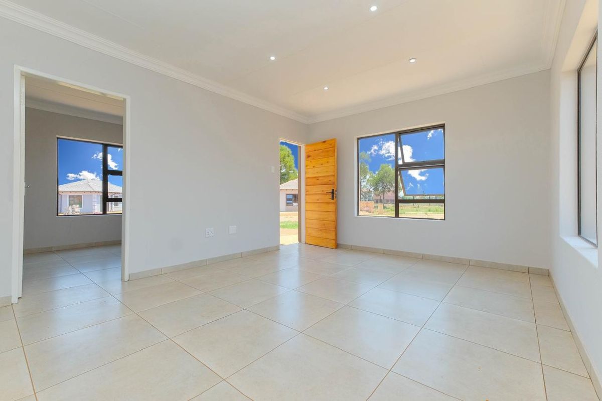 A bright, empty living area featuring neutral tiled flooring, recessed downlights, and modern aluminium window frames, offering a clean and versatile space.