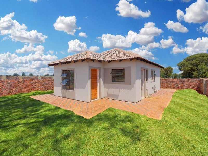 A well-maintained detached structure featuring a tiled roof, paved patio area, and a surrounding lawn enclosed by a brick boundary wall.