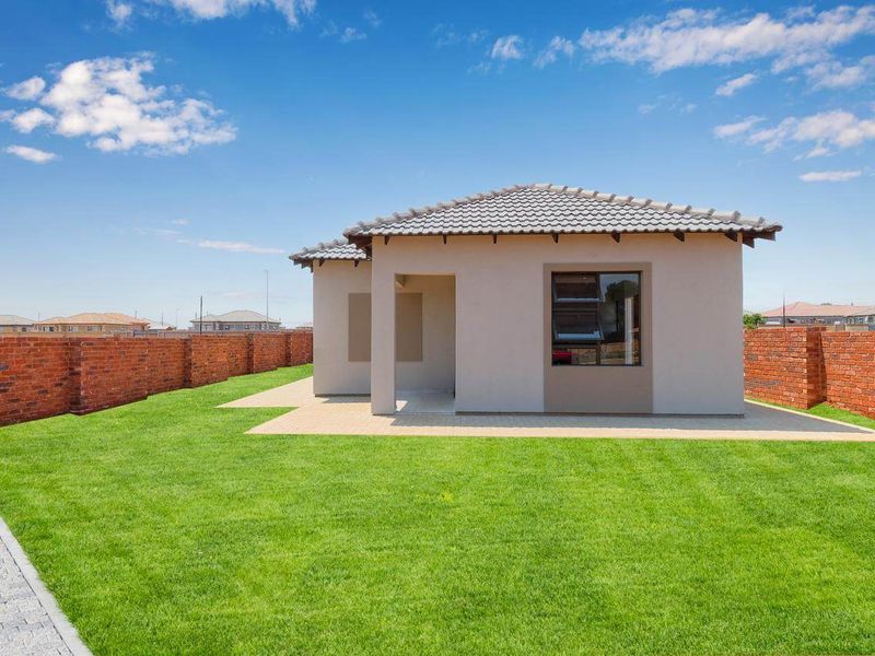 A well-maintained rear exterior view of a modern house featuring a paved patio, neat lawn, and secure brick boundary walls.