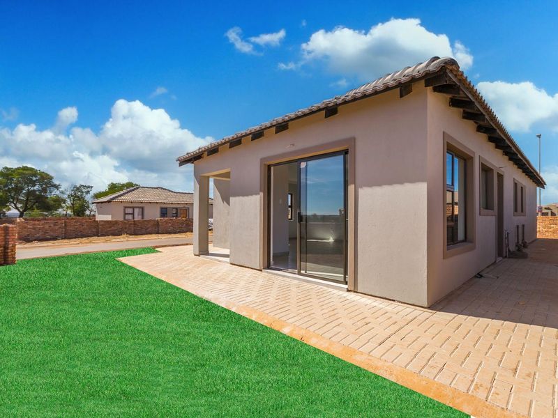Rear view of the house featuring a paved patio area, sliding glass doors, and a well-maintained lawn with brick boundary walling.