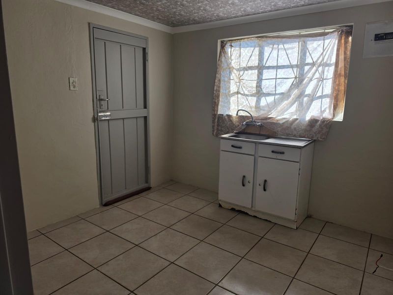 A functional scullery or utility area featuring tiled flooring, a single basin sink with built-in cabinetry, and a secure exterior door.