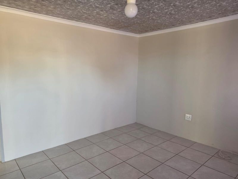 A clean, empty bedroom featuring neutral wall paint, tiled flooring, and a simple ceiling light fixture.