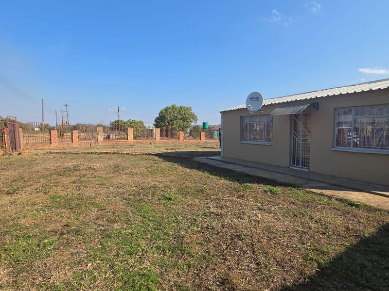Rear view of the property featuring a large open yard, brick perimeter wall, and a concrete apron along the building exterior.