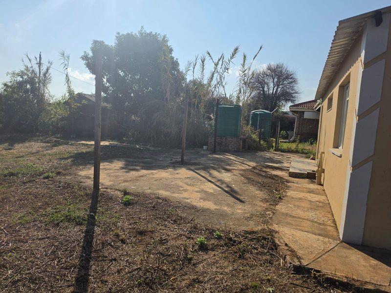 Rear exterior view of the property featuring a concrete patio area, water storage tanks on brick stands, and an expansive garden space.