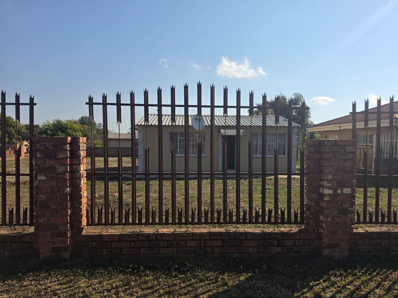 Front view of a single-story house featuring a brick and metal spike perimeter fence and a corrugated metal roof.