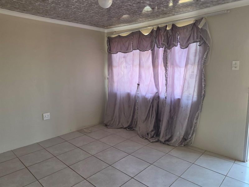 A vacant living room featuring neutral tiled flooring and a textured ceiling finish, providing a blank canvas for interior design.