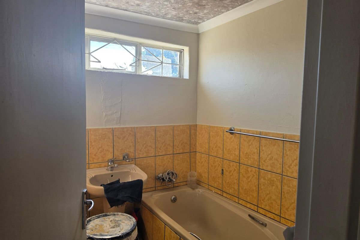 A functional bathroom featuring a pedestal basin, built-in bathtub, and tiled splashback, currently requiring cosmetic updates and maintenance to improve its overall condition.