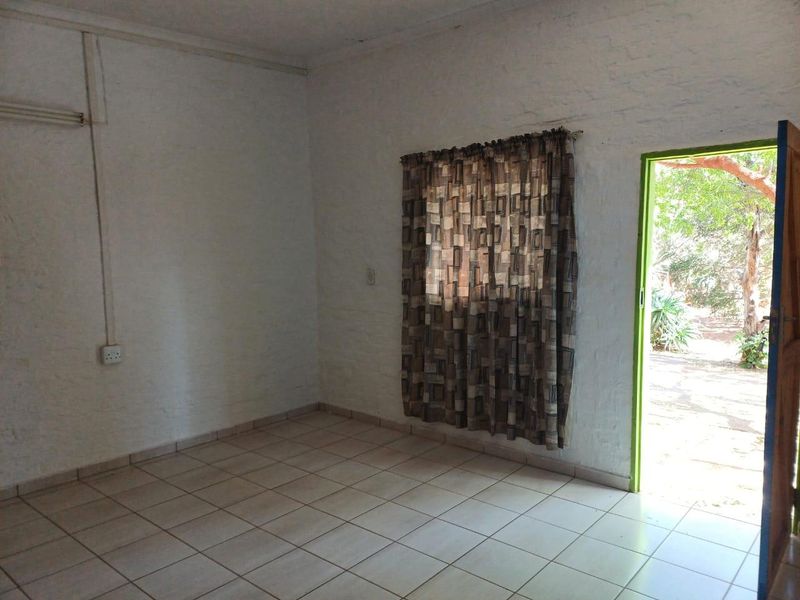An empty living area featuring tiled flooring, textured brick walls, and direct access to an outdoor space.