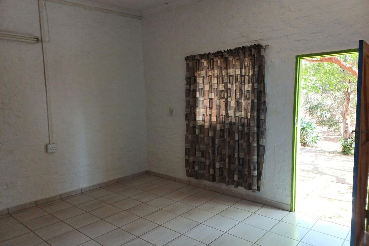 An empty living area featuring tiled flooring, textured brick walls, and direct access to an outdoor space.
