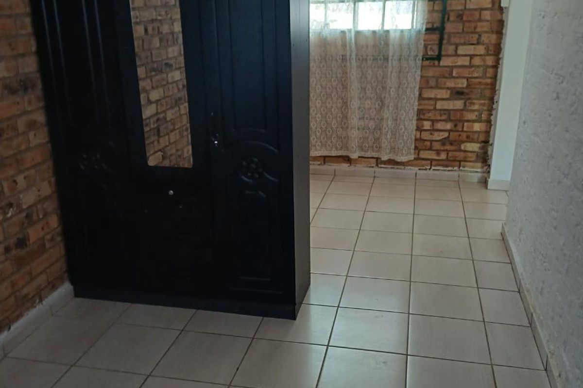 A bedroom featuring exposed brick walls, ceramic floor tiling, and security burglar bars on the window.