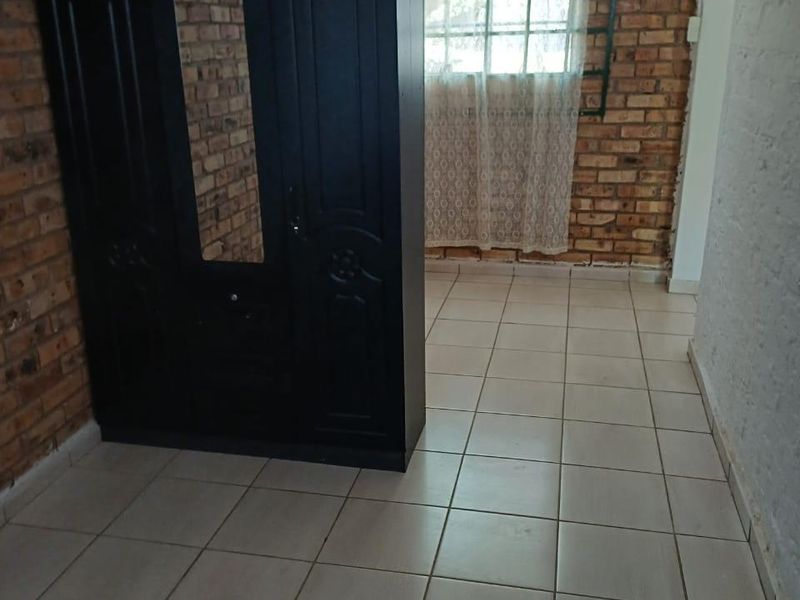 A bedroom featuring exposed brick walls, ceramic floor tiling, and security burglar bars on the window.