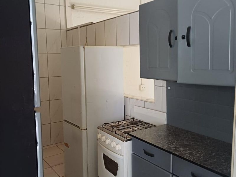 A functional kitchen featuring grey cabinetry, a gas stove, and tiled surfaces, offering a practical layout with potential for modern cosmetic updates.