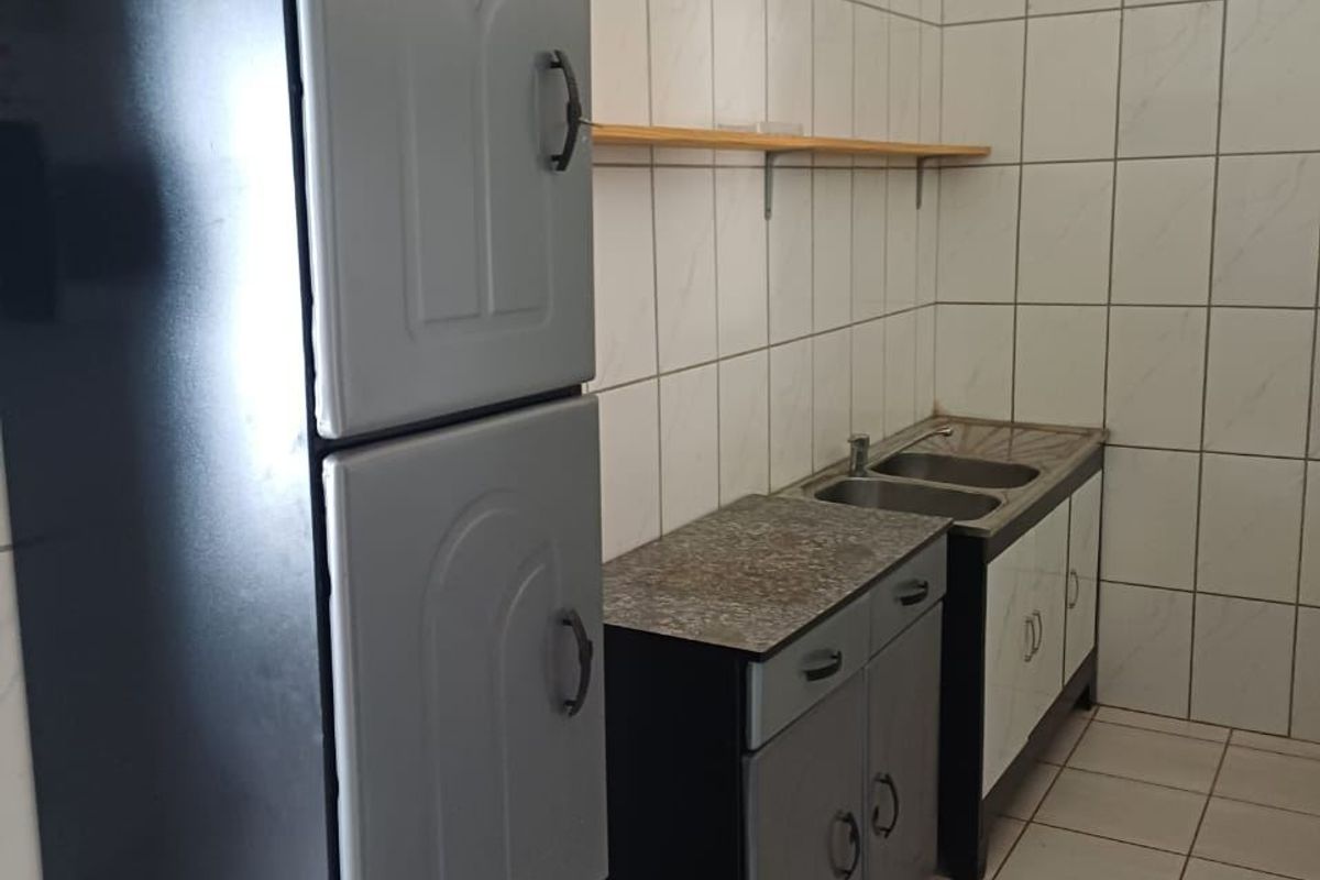A functional kitchen area featuring tiled walls and floors, built-in cabinetry with a double basin sink, and a wall-mounted storage shelf.