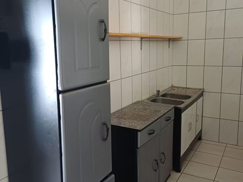A functional kitchen area featuring tiled walls and floors, built-in cabinetry with a double basin sink, and a wall-mounted storage shelf.