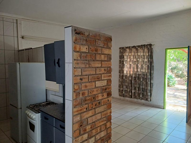 Open plan kitchen and living area featuring an exposed brick partition wall, tiled flooring, and direct access to the outdoor garden area.