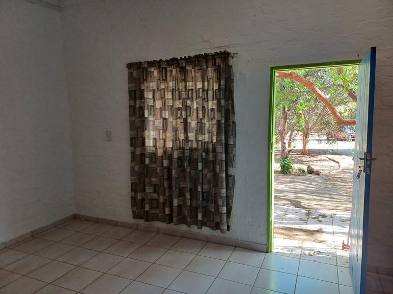 An empty living area featuring tiled flooring, textured painted brick walls, and direct access to the outdoor garden space.