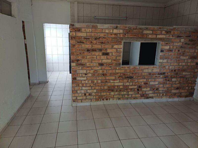 An empty open-plan area featuring an exposed brick partition wall and ceramic floor tiling, requiring renovation to improve the overall finish and aesthetic.