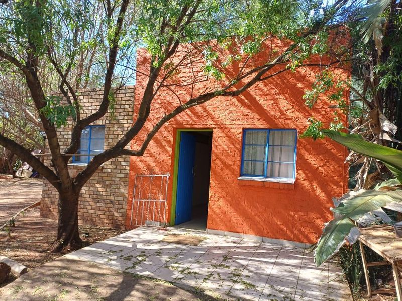 Exterior view of a small residential unit featuring a textured orange brick facade, blue steel window frames, and a tiled entrance patio.