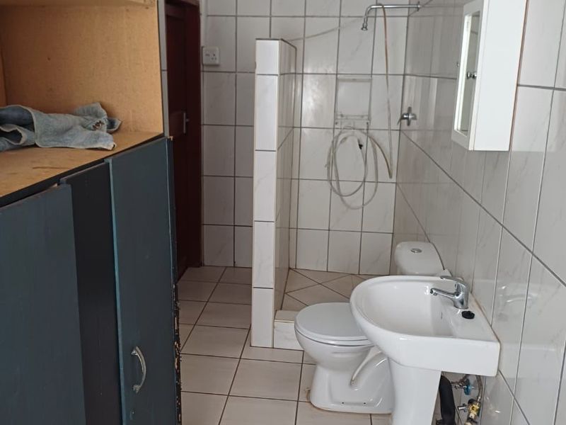 A functional bathroom featuring a pedestal basin, toilet, and shower area with full-height wall tiling and built-in storage cabinetry.