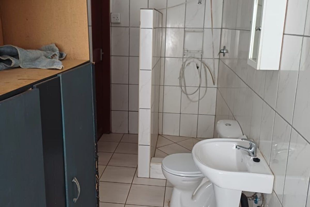 A functional bathroom featuring a pedestal basin, toilet, and shower area with full-height wall tiling and built-in storage cabinetry.