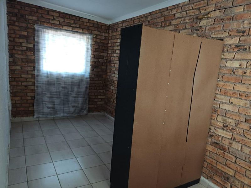 Bedroom featuring exposed brick walls and tiled flooring, offering a rustic aesthetic that could be enhanced with modern finishes and updated lighting.