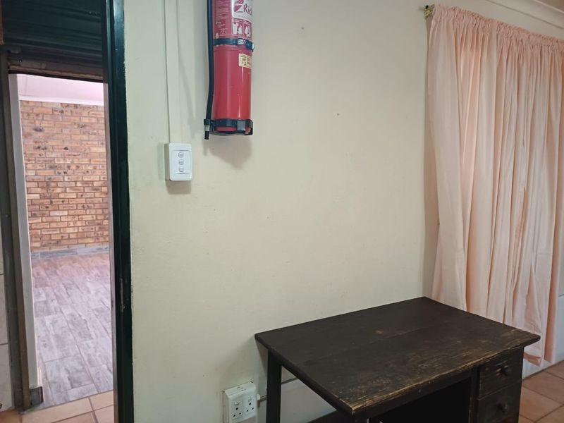 A functional hallway area featuring a wall-mounted fire extinguisher, electrical points, and access to an adjacent room with exposed brickwork.