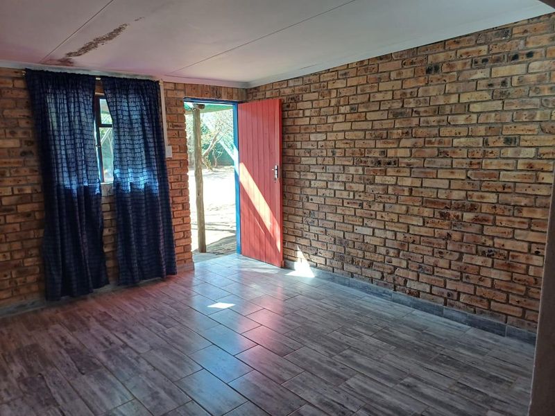 An empty living area featuring exposed brick walls, tiled flooring, and direct access to the exterior through a timber door.