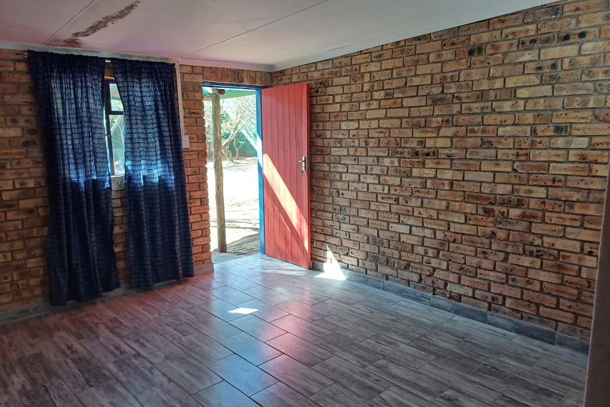 An empty living area featuring exposed brick walls, tiled flooring, and direct access to the exterior through a timber door.