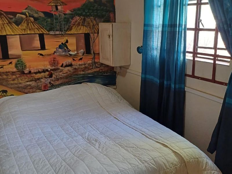 A bedroom featuring tiled flooring, a wall-mounted storage cabinet, and security burglar bars on the window.