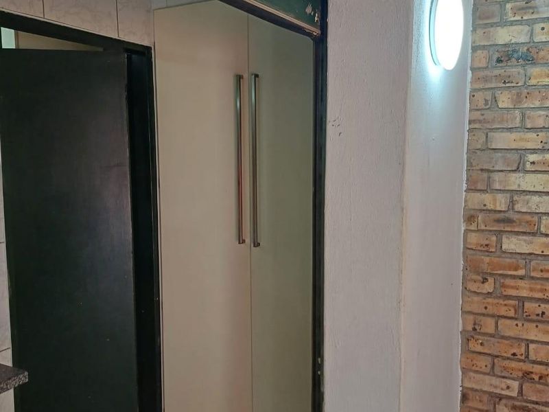 A functional hallway featuring built-in storage cupboards, an exposed brick feature wall, and tiled flooring with a wall-mounted light fixture.