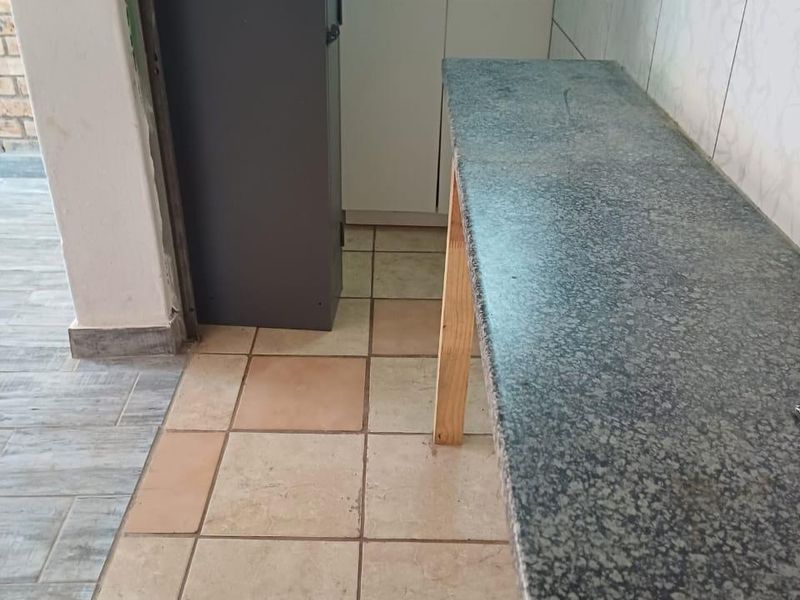 A compact kitchen area featuring granite countertops, a stainless steel sink, and tiled finishes, currently vacant and ready for updates.