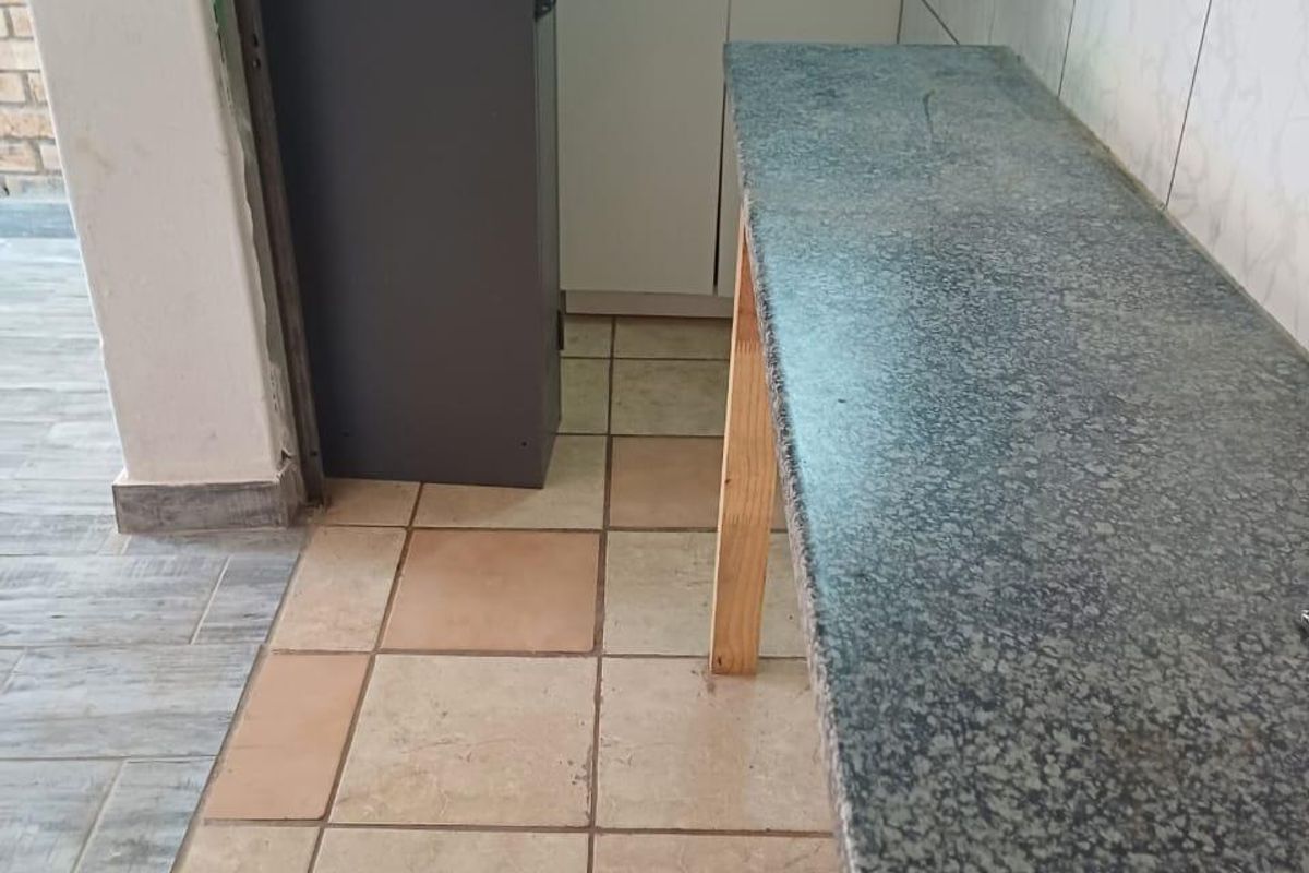 A compact kitchen area featuring granite countertops, a stainless steel sink, and tiled finishes, currently vacant and ready for updates.