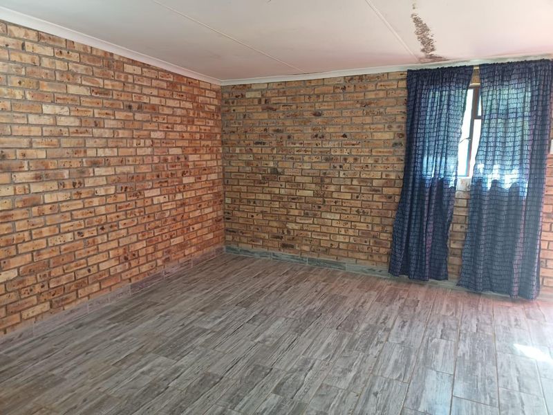 An empty bedroom featuring exposed brick walls and wood-look tile flooring, with visible water damage on the ceiling requiring attention.