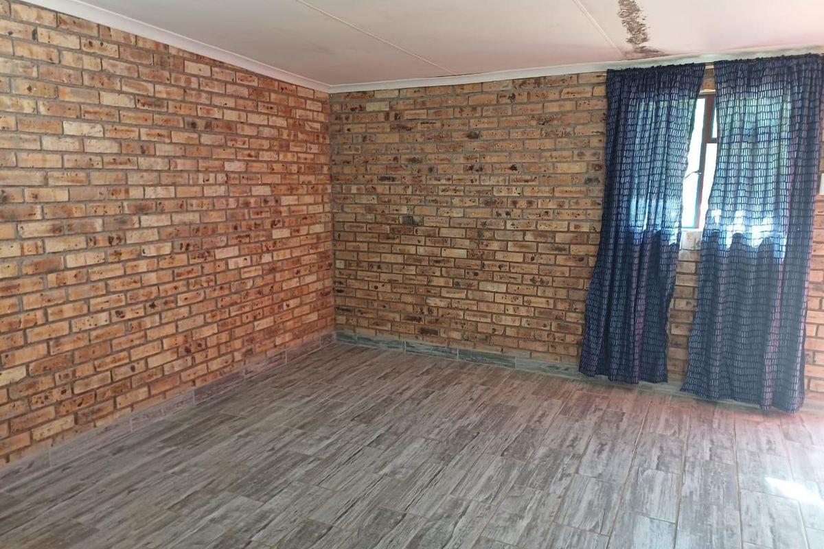 An empty bedroom featuring exposed brick walls and wood-look tile flooring, with visible water damage on the ceiling requiring attention.
