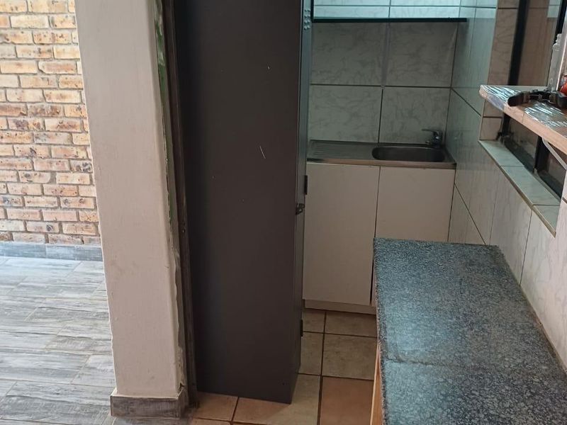 A compact scullery area featuring a stainless steel sink, granite countertop, and tiled splashbacks, providing functional prep space adjacent to an outdoor area.