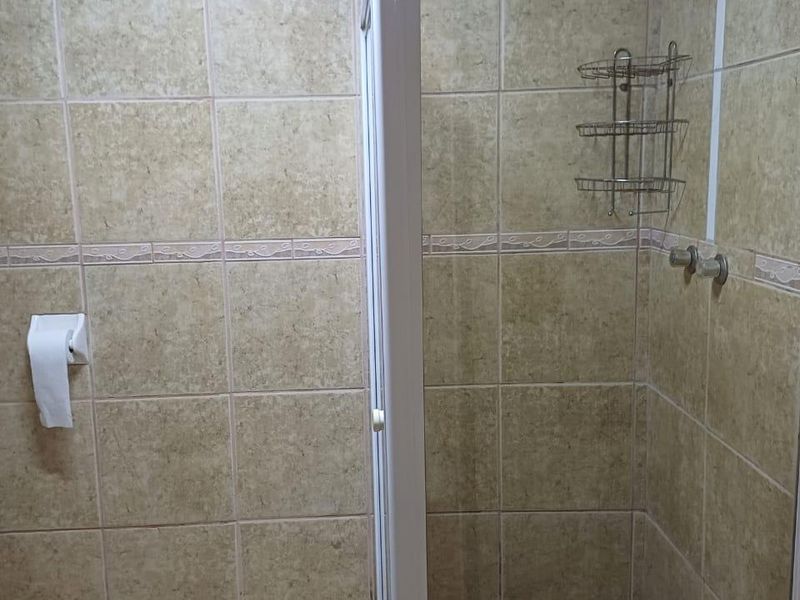 A functional bathroom featuring a glass-enclosed shower with neutral ceramic wall and floor tiling.