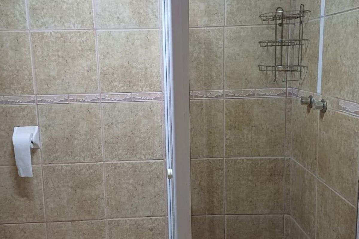 A functional bathroom featuring a glass-enclosed shower with neutral ceramic wall and floor tiling.