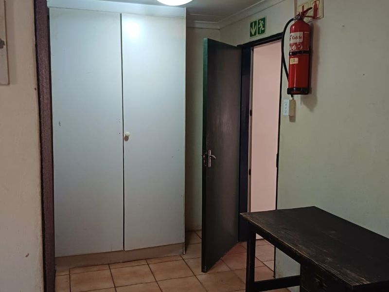 A functional hallway area featuring built-in storage cupboards, tiled flooring, and essential safety equipment including a fire extinguisher and emergency signage.