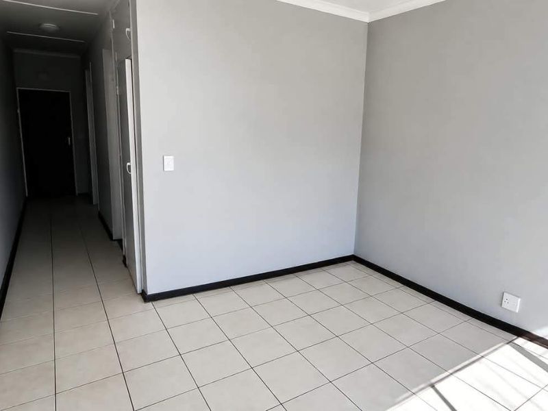 An empty, neutrally painted living area featuring tiled flooring and a connecting hallway, providing a clean and versatile space for interior design.