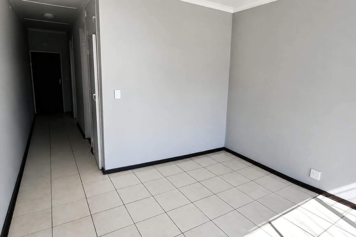 An empty, neutrally painted living area featuring tiled flooring and a connecting hallway, providing a clean and versatile space for interior design.