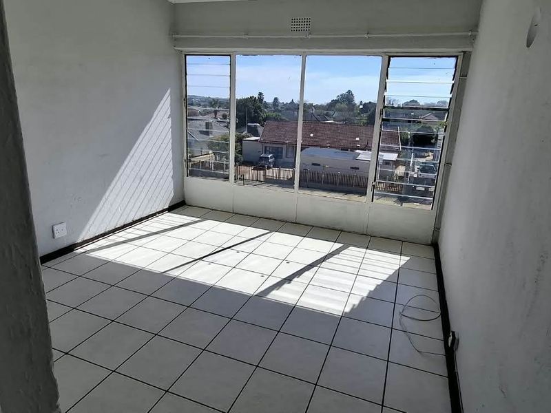 An empty bedroom featuring tiled flooring and large windows with natural light, offering a clear view of the surrounding neighborhood.