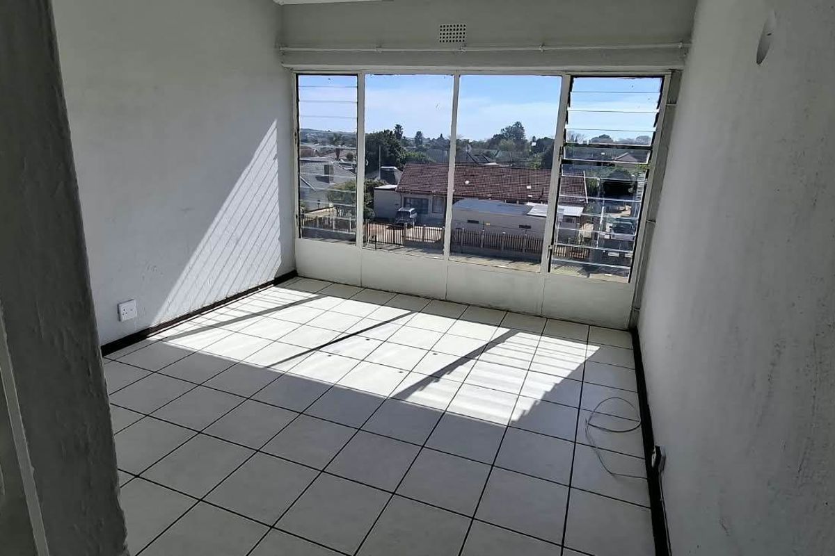 An empty bedroom featuring tiled flooring and large windows with natural light, offering a clear view of the surrounding neighborhood.