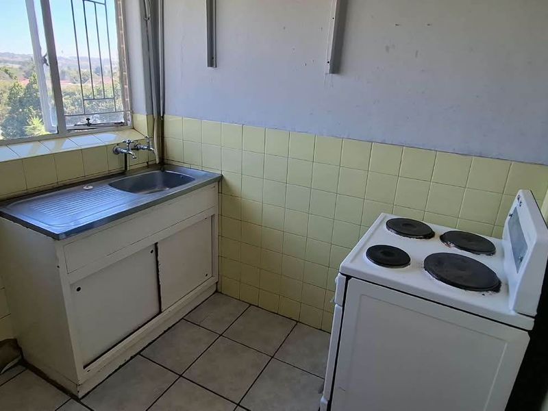 A compact, dated kitchen featuring a stainless steel sink, tiled splashbacks, and an electric stove, offering a functional space ready for modernization.