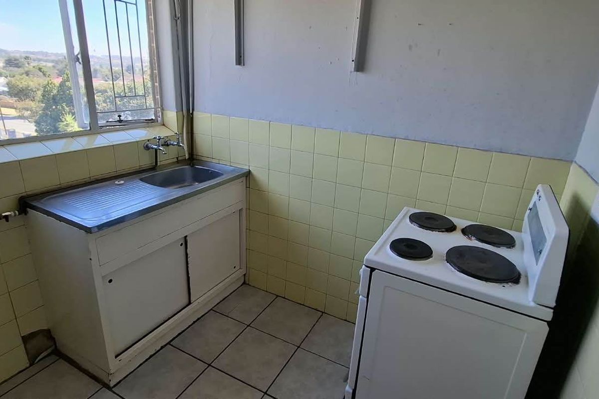 A compact, dated kitchen featuring a stainless steel sink, tiled splashbacks, and an electric stove, offering a functional space ready for modernization.