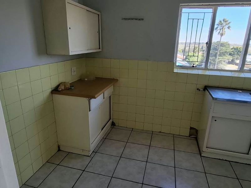 A dated kitchen featuring original cabinetry, a stainless steel sink, tiled backsplash, and tiled flooring, offering significant potential for a modern renovation.
