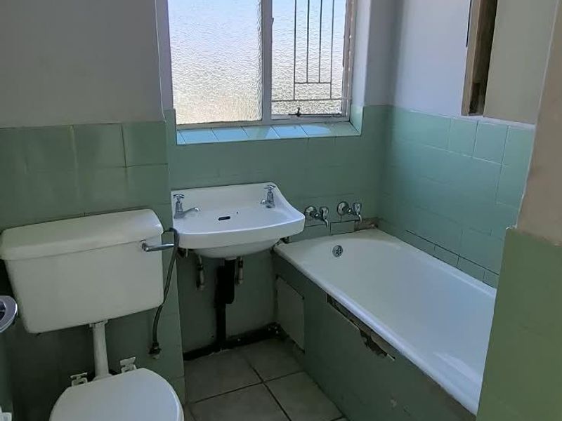 A dated bathroom featuring a bathtub, pedestal sink, and toilet with original green wall tiling and ceramic floor tiles.