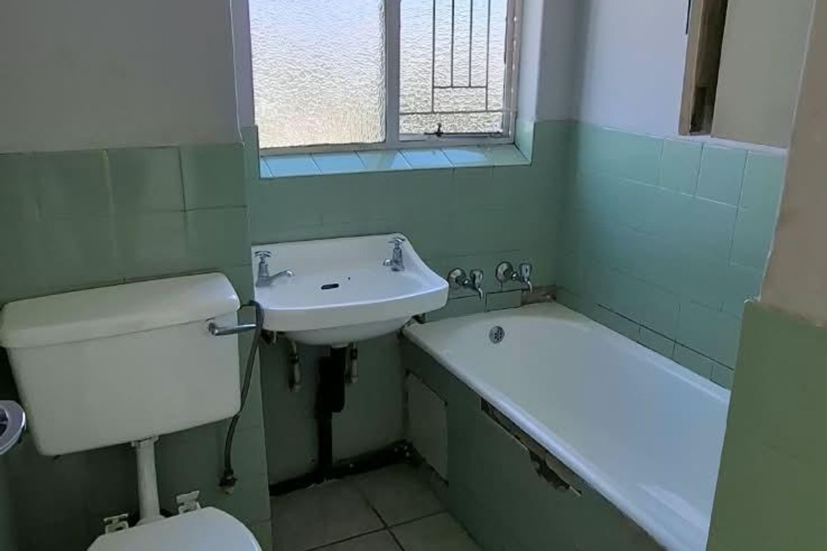 A dated bathroom featuring a bathtub, pedestal sink, and toilet with original green wall tiling and ceramic floor tiles.
