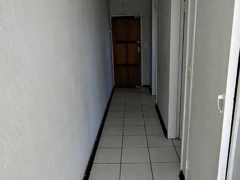 A narrow residential hallway featuring tiled flooring, built-in storage cupboards, and access to multiple rooms.