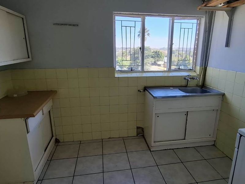A dated kitchen featuring tiled splashbacks, a stainless steel sink, and built-in cabinetry, offering significant potential for renovation and modernization.